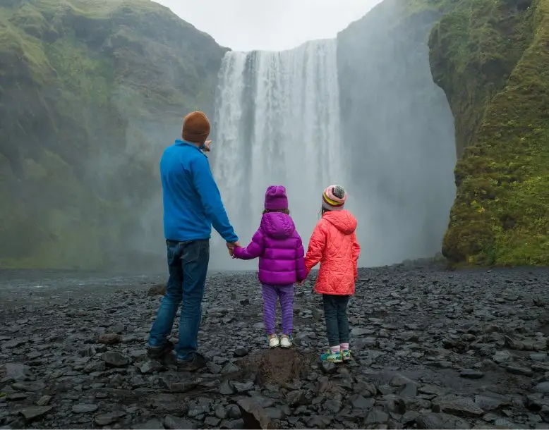 One parent with two children look at a waterfall