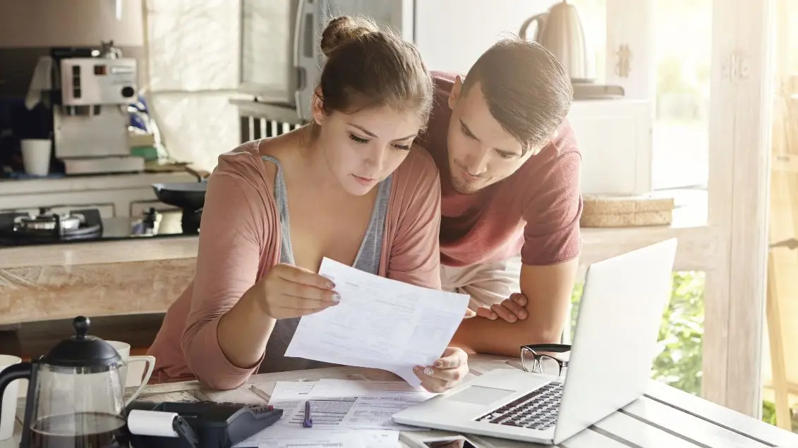 A couple reviews their employee benefits in their kitchen over a cup of coffee